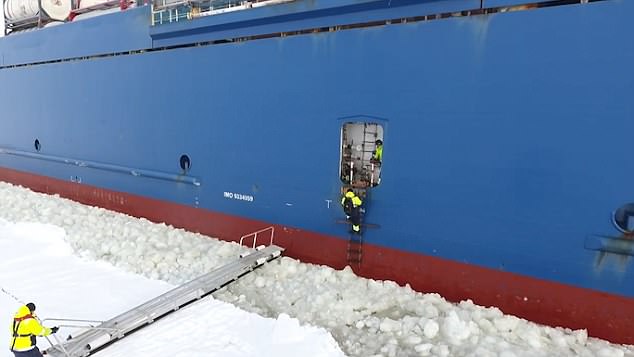 With no life jacket on, the sailor waits until the perfect moment to cling onto a rope ladder and climb through a small hatch on the side of the cargo ship